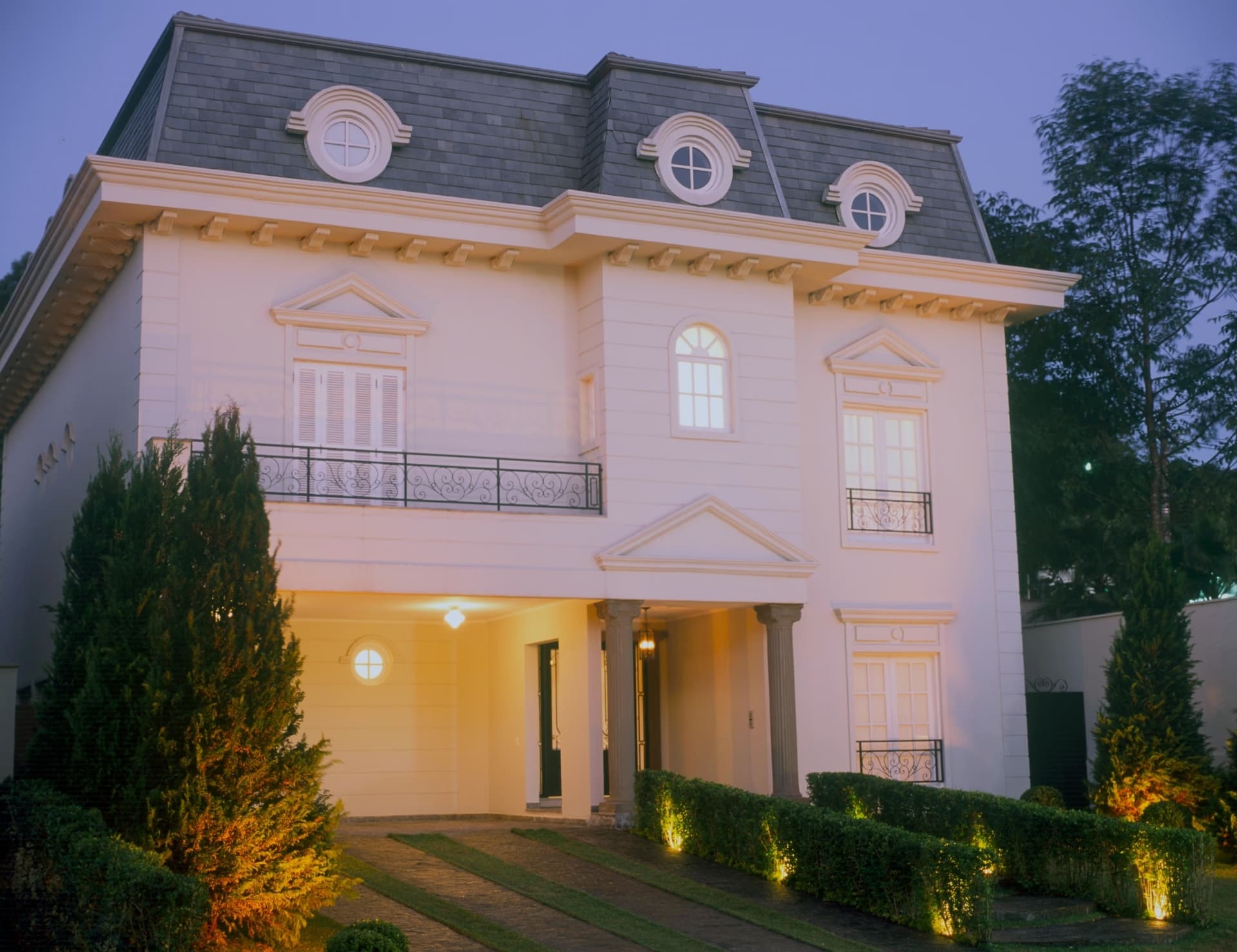 Fachada residencial integrada ao paisagismo francês ao entardecer